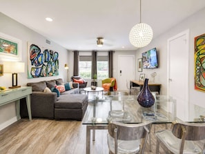 A modern living room with a glass dining table, a sofa, a coffee table, and a TV.