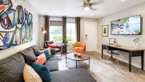 A modern living room with a sofa, chairs, a desk, and a television. - Modern Myers Park 1BR · Ground Floor · Free Parking near Atrium CMC & Uptown (Charlotte)
