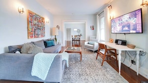 A living room with a grey sofa, a coffee table, and a TV on a stand. There is a dining area with a table and chairs. - Modern 2BR Elizabeth Suites | Parking & Private Balcony | near Uptown (Charlotte)