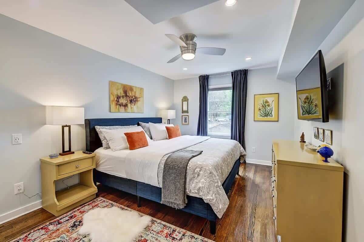 A bedroom with a bed, bedside tables, a dresser, a ceiling fan, and artwork on the walls.