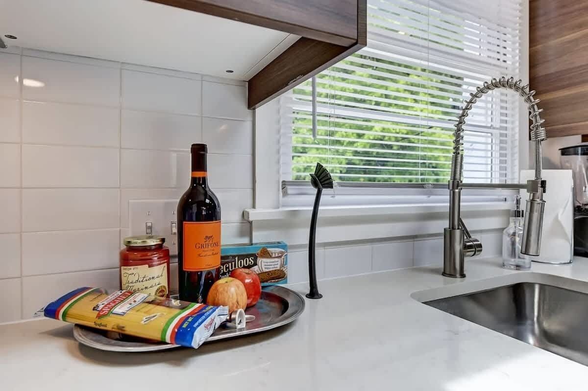 A kitchen with a modern faucet, a bottle of wine, a jar of sauce, a pumpkin, and a bag of pasta on the counter.