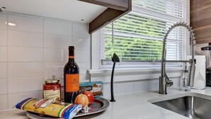 A kitchen with a modern faucet, a bottle of wine, a jar of sauce, a pumpkin, and a bag of pasta on the counter.