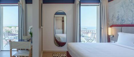Quarto de hotel com cama, escrivaninha com cadeira, espelho e vista para a cidade.