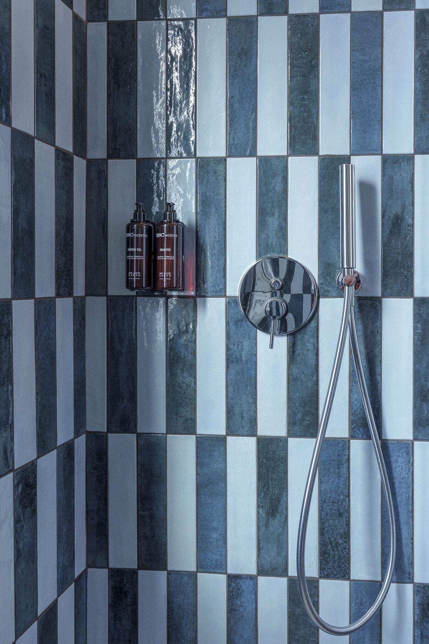 Un baño con pared de baldosas a cuadros, cabezal de ducha de mano y dos botellas de gel de ducha y champú.