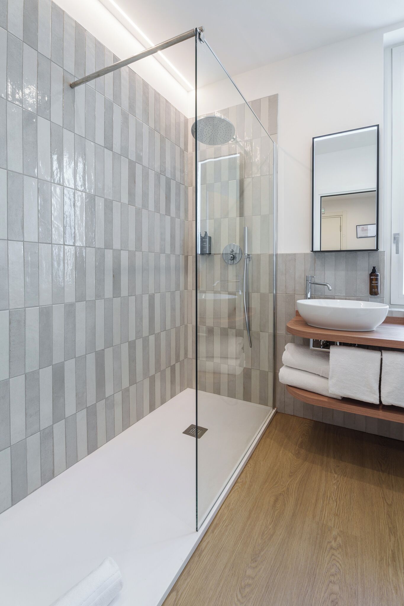 A modern bathroom with a glass-enclosed shower, a white sink, and a wooden vanity.