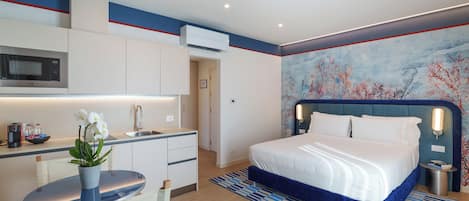 A modern hotel room with a bed, a desk, a microwave, and a kitchen area.