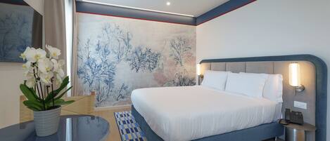 A modern hotel room with a large bed, bedside tables, a desk, and a decorative wall.