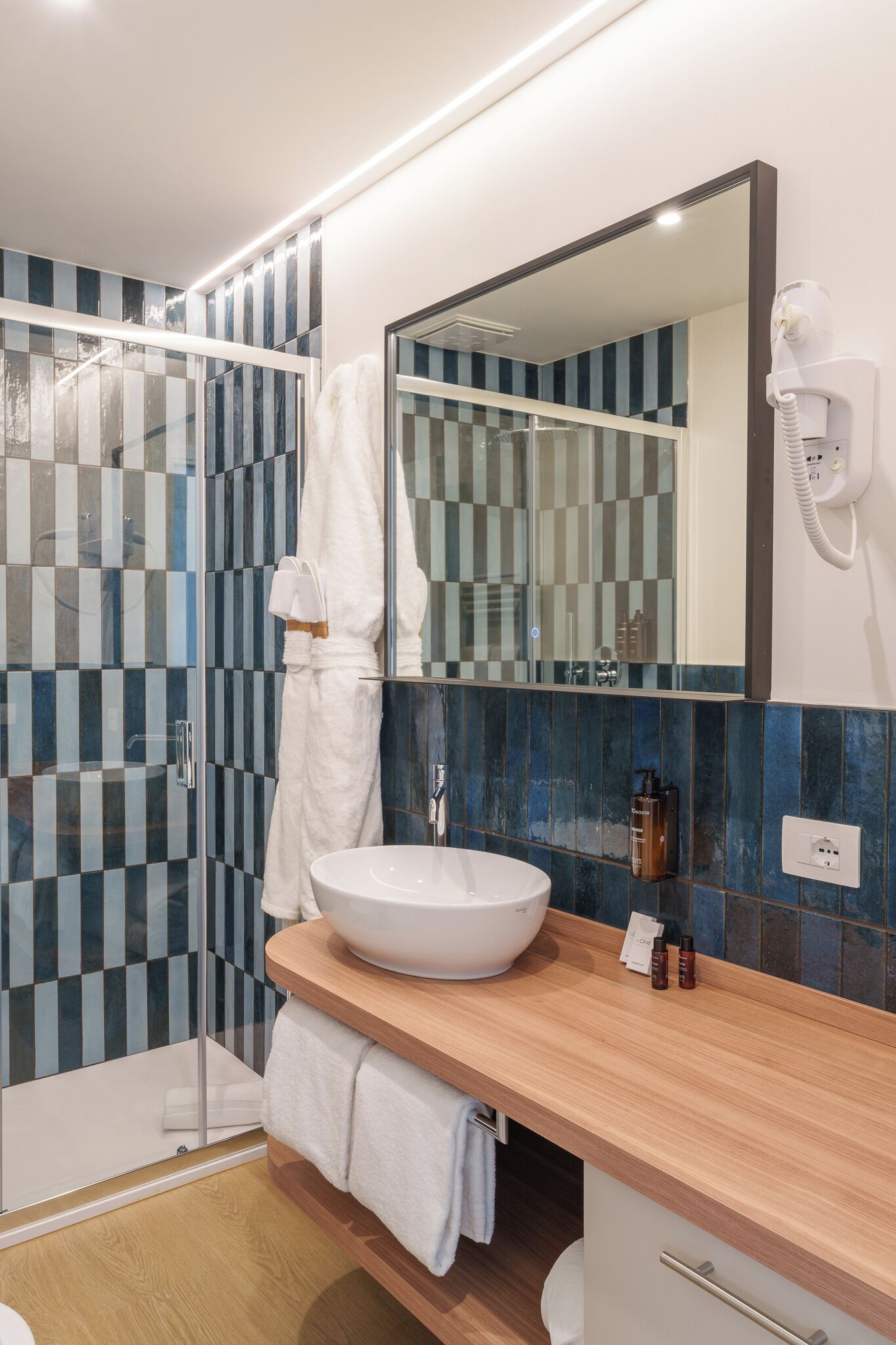 Ein modernes Badezimmer mit einem großen Spiegel, einem weißen Waschbecken und einer Duschkabine aus Glas.