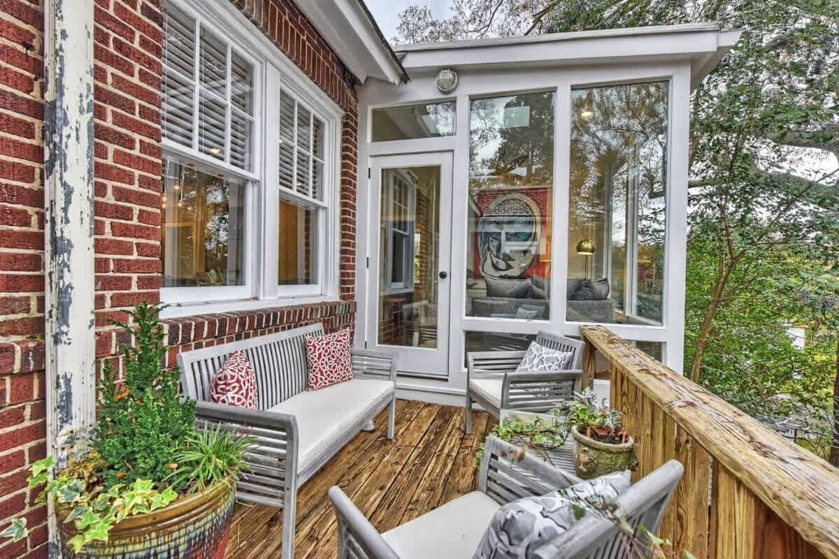 A cozy outdoor seating area with a wooden deck, a brick wall, and a glass door leading to a garden.