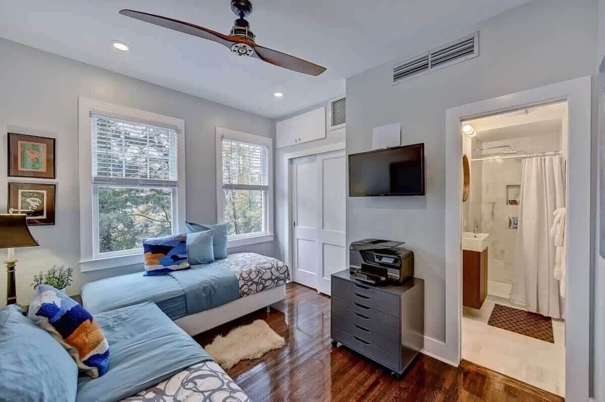 A bedroom with a bed, a ceiling fan, a TV, and a bathroom visible through an open door.