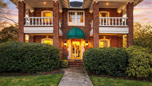 A two-story brick house with a front porch, a green awning over the entrance, and a pathway leading to the door.
