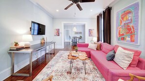 A living room with a pink sofa, a wooden coffee table, a ceiling fan, and a flat-screen TV.