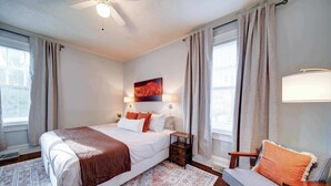 A bedroom with a bed, bedside tables, a chair, a rug, and a painting on the wall.