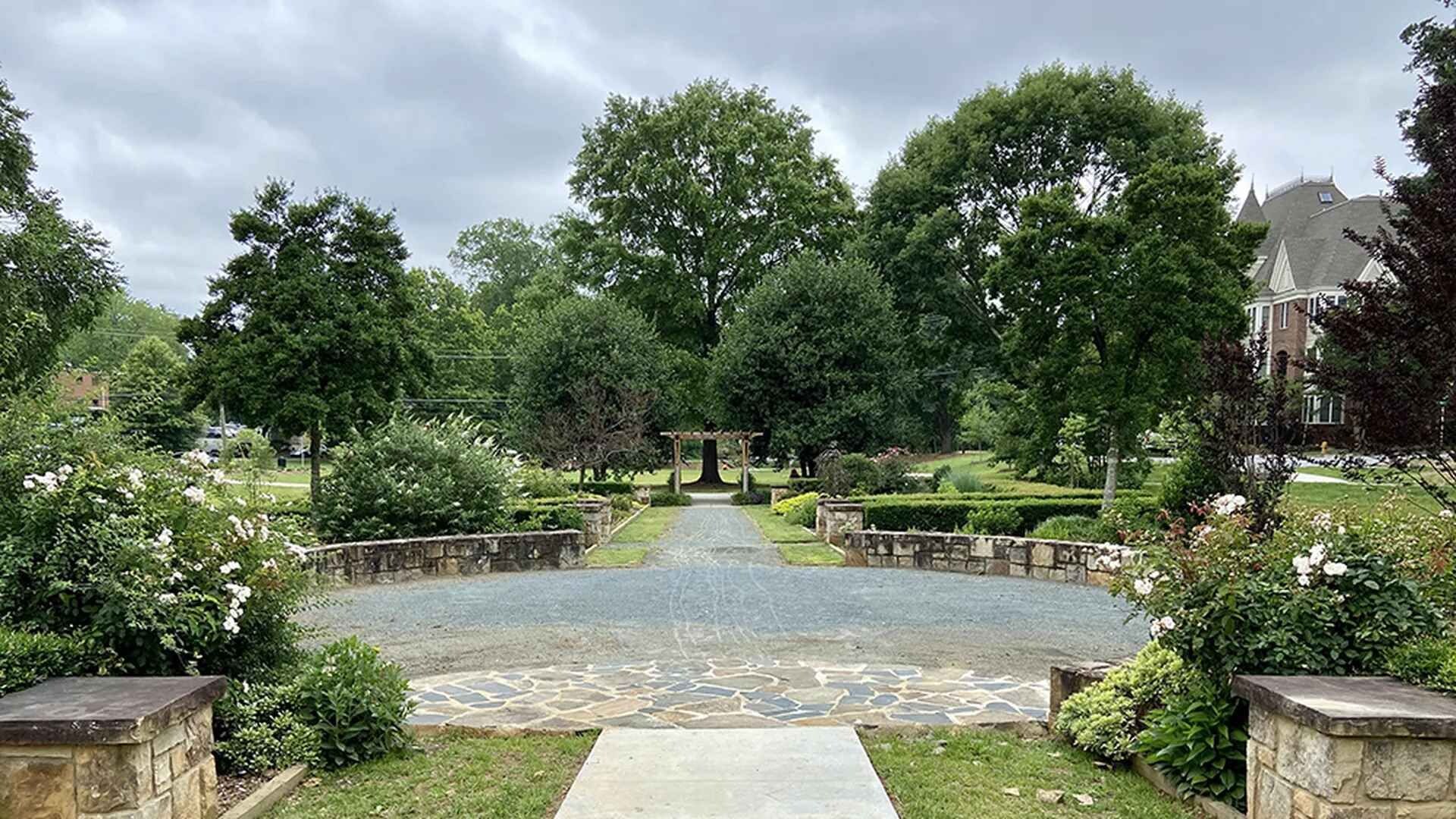 A garden pathway leading to a central archway surrounded by lush greenery and stone walls.