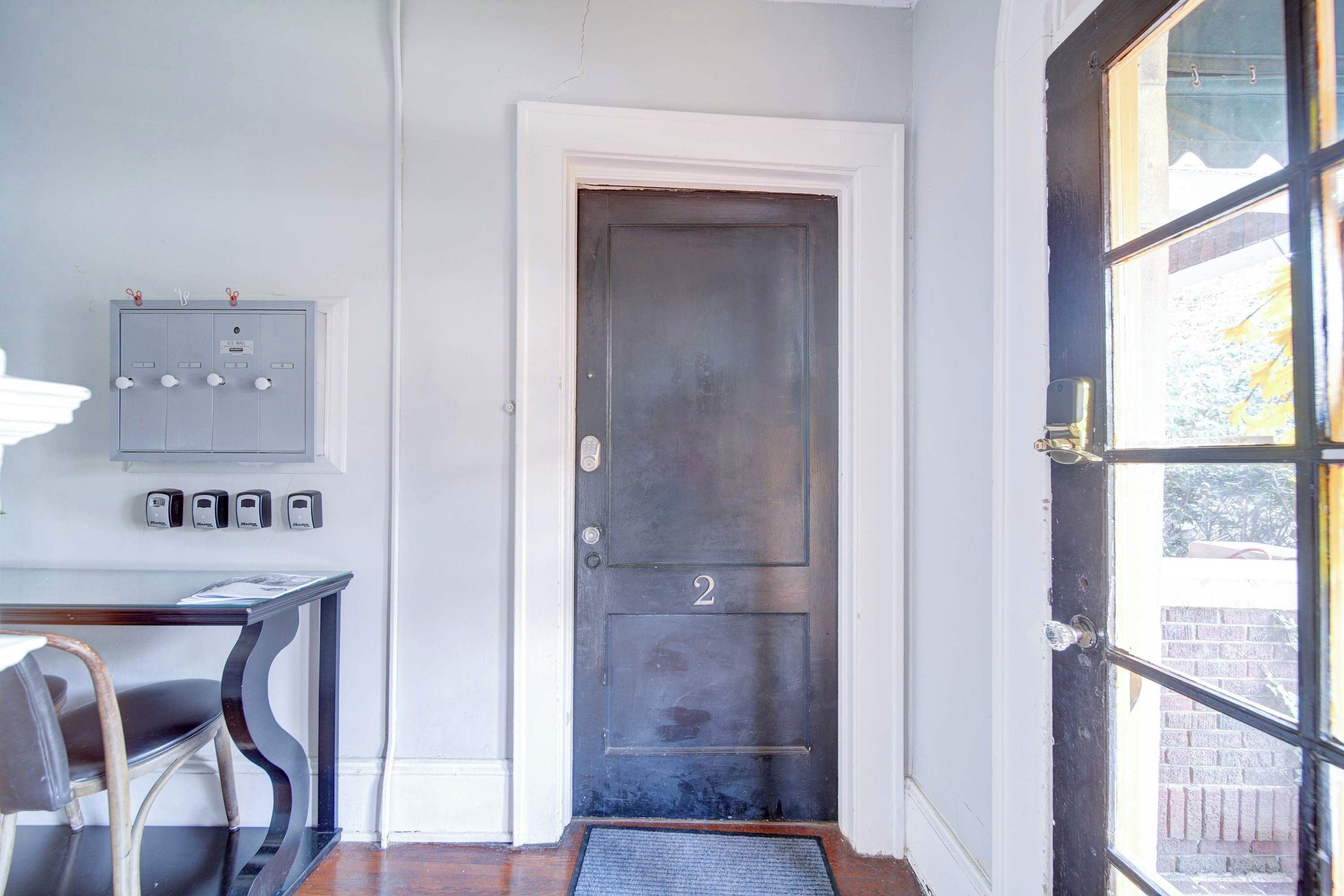 Uma porta com placa de número, um quadro elétrico fixado na parede e uma porta de vidro com vista.