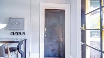 Uma porta com placa de número, um quadro elétrico fixado na parede e uma porta de vidro com vista.
