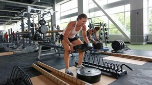 A gym with weightlifting equipment, including barbells and weight plates, and a person performing a deadlift.