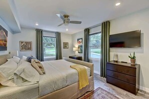 A bedroom with a bed, a nightstand, a dresser, a TV, and a ceiling fan.