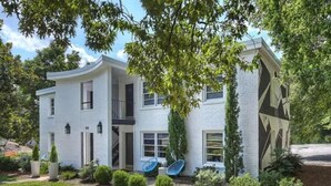 Une maison moderne à deux étages, dotée d’une façade incurvée, de plusieurs antennes paraboliques et d’un jardin bien entretenu.