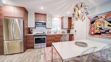 A modern kitchen with stainless steel appliances, wooden cabinets, and a dining area with a white table and clear chairs.