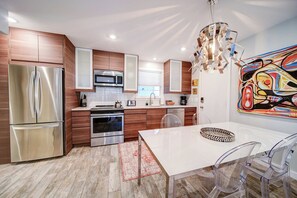 Eine moderne Küche mit Edelstahlgeräten, Holzschränken und einem Essbereich mit einem weißen Tisch und transparenten Stühlen.