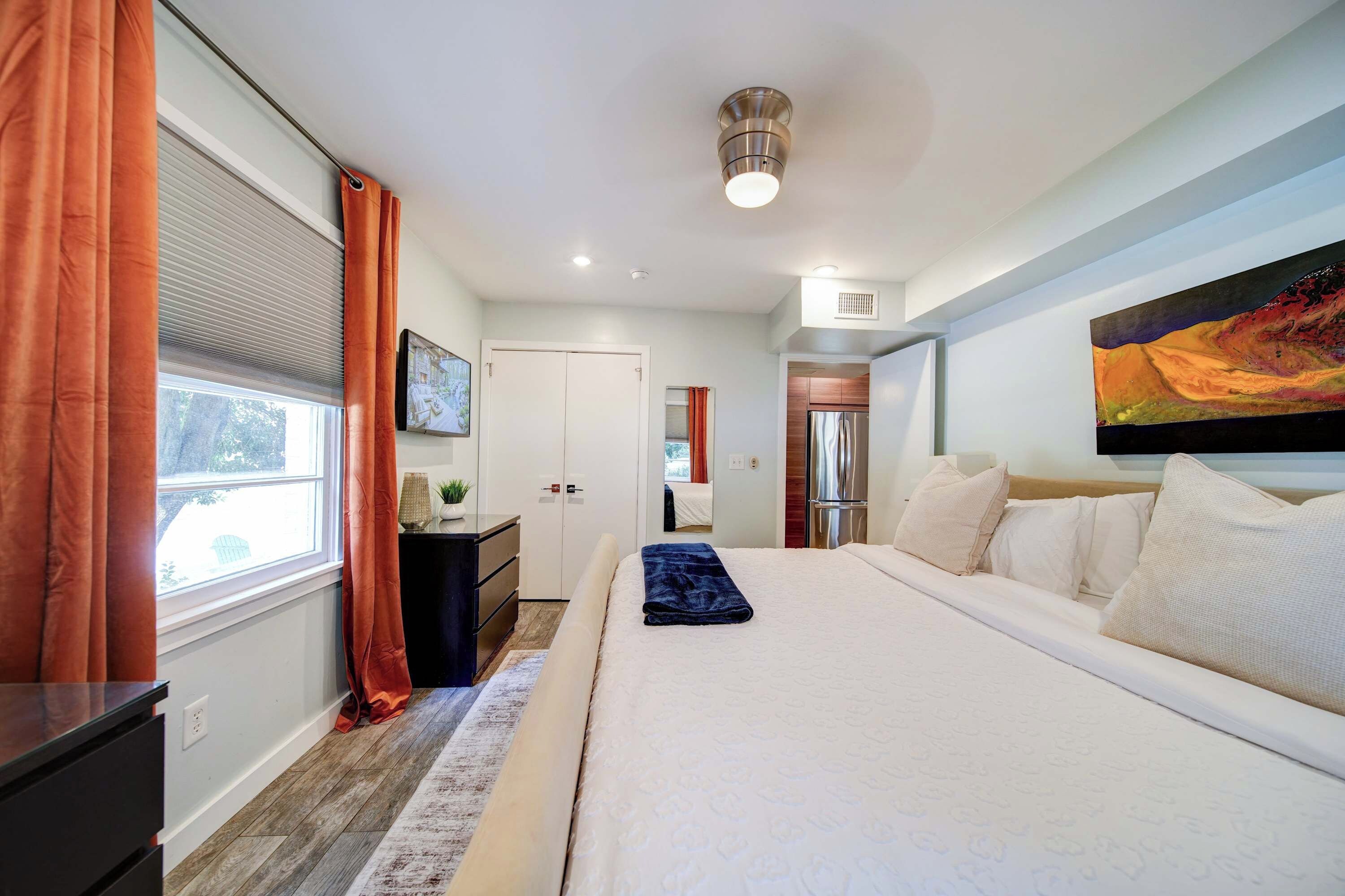 A modern bedroom with a large bed, a desk, and a window with curtains.