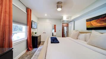 A modern bedroom with a large bed, a desk, and a window with curtains.