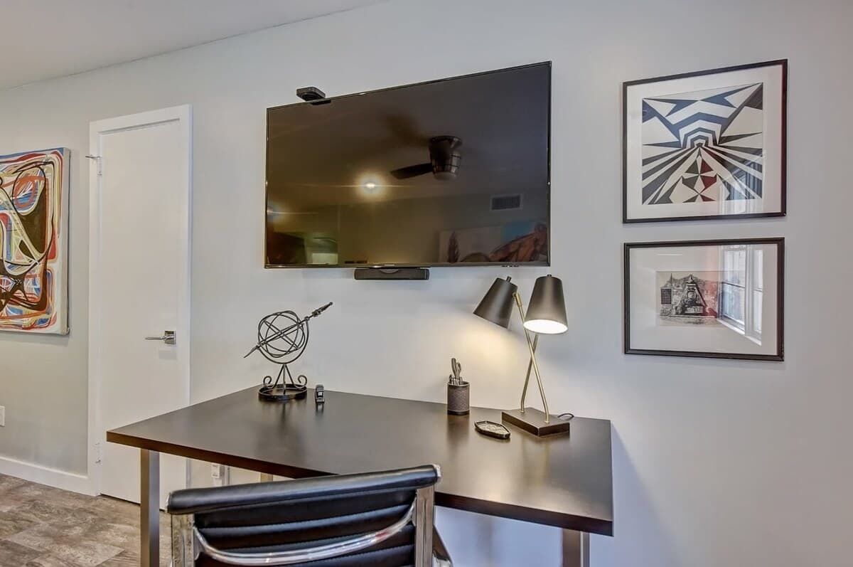 A modern office space with a desk, chair, and a large flat-screen TV mounted on the wall.