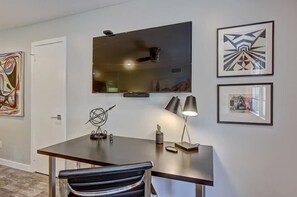 Ein moderner Büroraum mit Schreibtisch, Stuhl und einem großen Flachbildfernseher an der Wand.