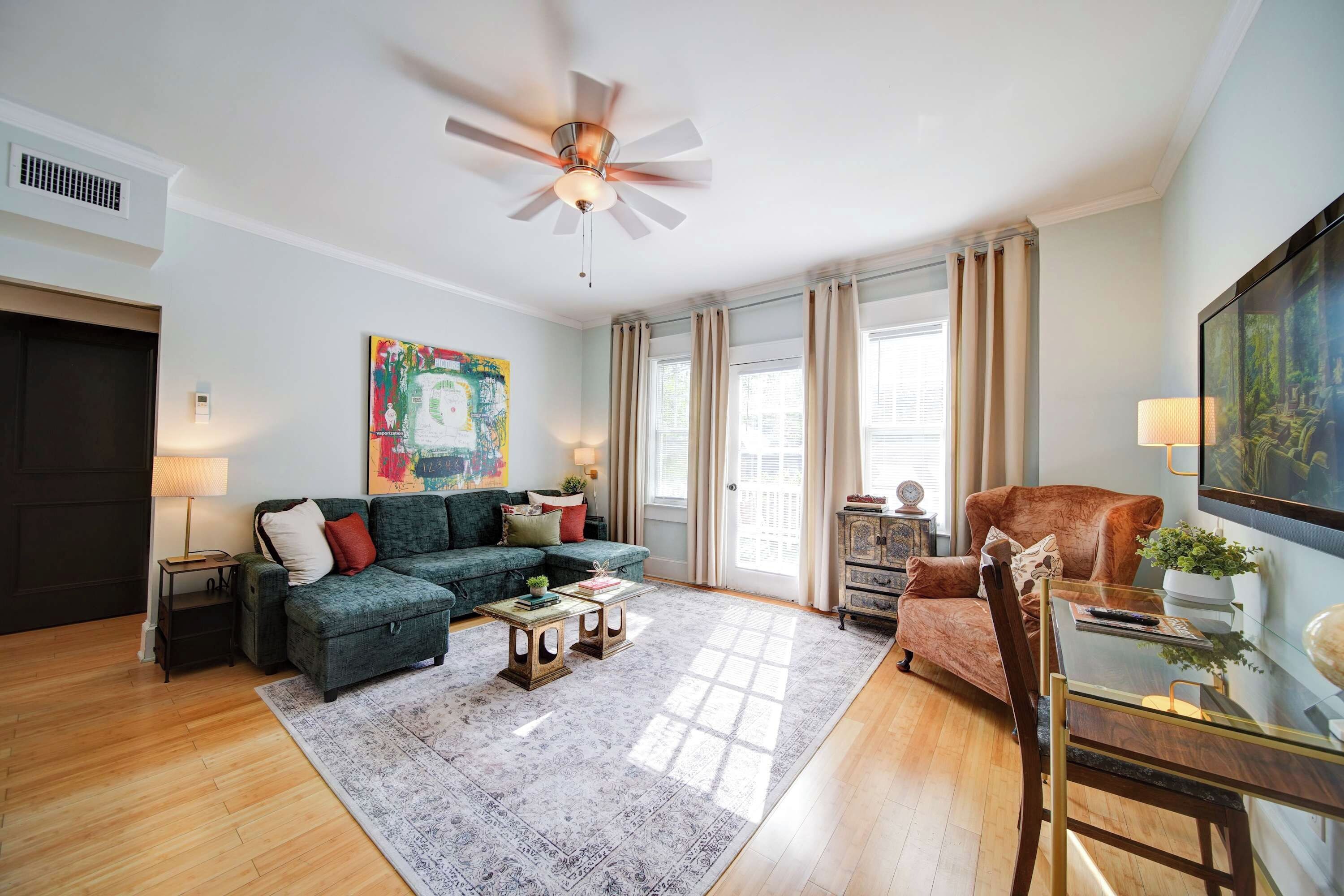 A living room with a sectional sofa, a coffee table, a glass table, a television, and a ceiling fan.