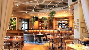Un restaurante con zona de bar, asientos y plantas colgantes.