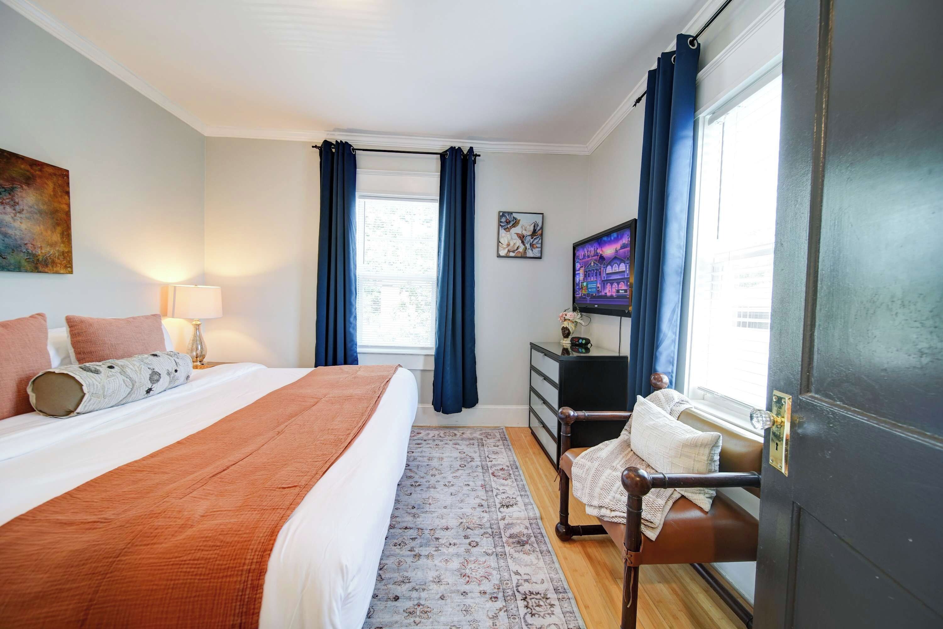 A hotel room with a bed, a desk, a chair, a TV, and a window with curtains.