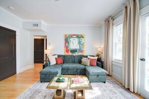 A living room with a sectional sofa, a coffee table, and a colorful abstract painting. - The Home Collection: King Suite with Private Balcony near Atrium & South End (Charlotte)
