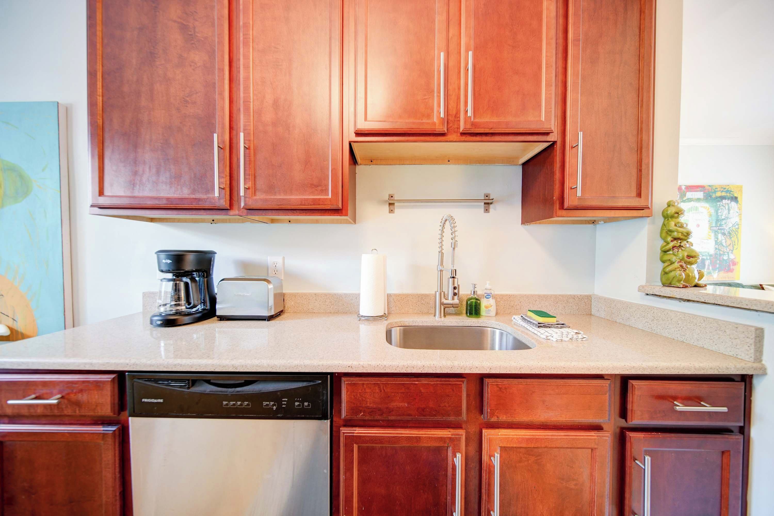 A kitchen with wooden cabinets, a coffee maker, a toaster, a dish soap dispenser, and a dish rack.
