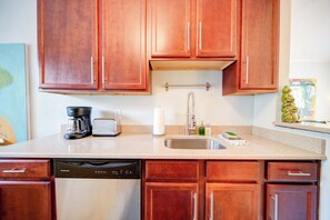 A kitchen with wooden cabinets, a coffee maker, a toaster, a dish soap dispenser, and a dish rack. - The Home Collection: King Suite with Private Balcony near Atrium & South End (Charlotte)