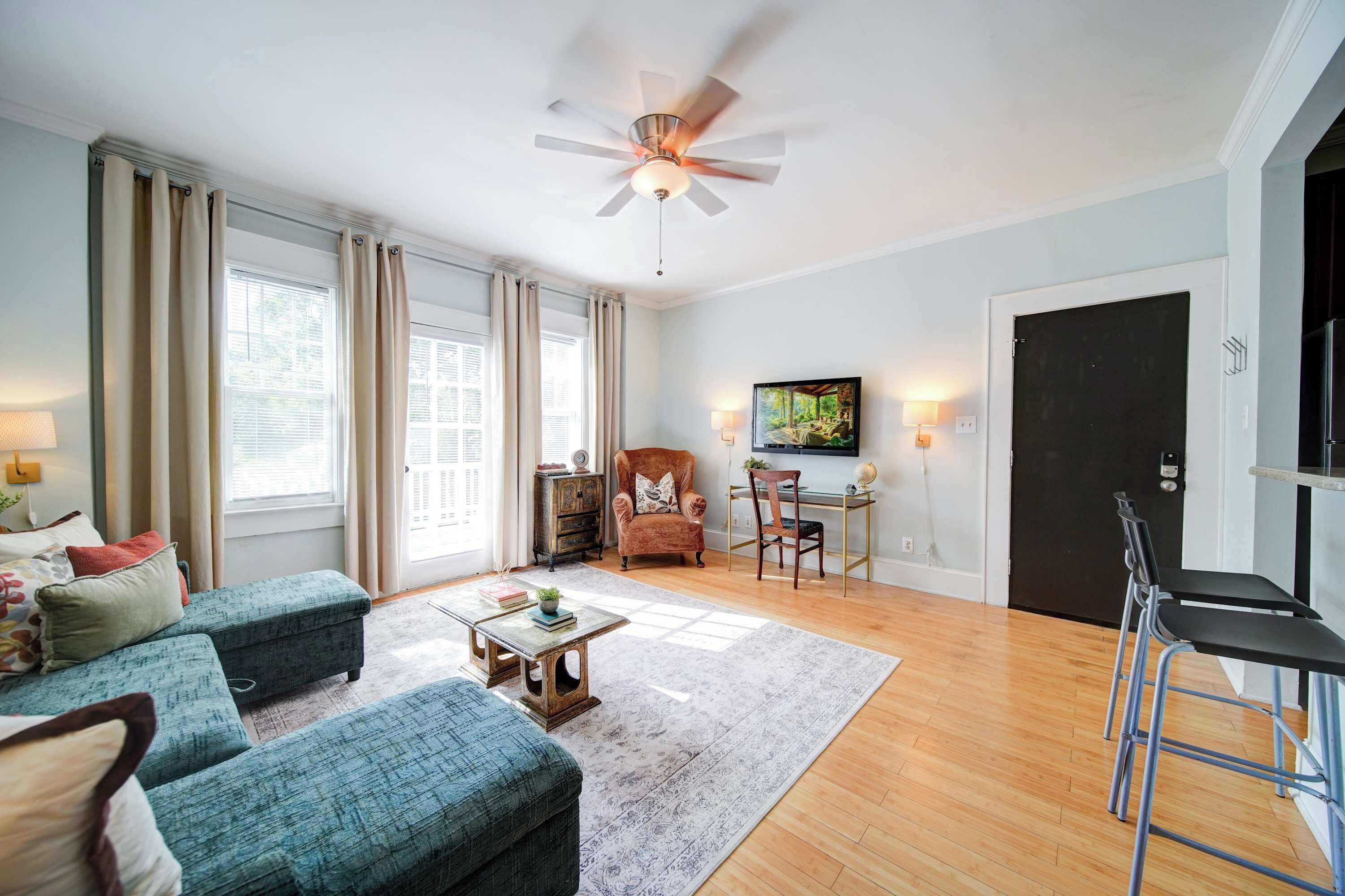 A spacious living room with a ceiling fan, a sofa set, a coffee table, and a TV mounted on the wall.