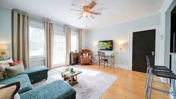 A spacious living room with a ceiling fan, a sofa set, a coffee table, and a TV mounted on the wall.