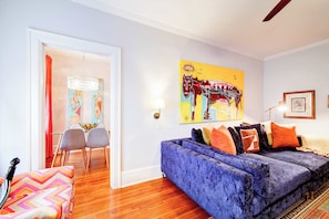A living room with a blue sofa, a dining area with chairs, and a painting on the wall.