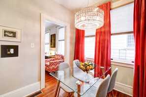 A dining area with a glass table, chairs, a chandelier, and red curtains.
