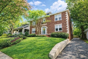 A two-story brick house with a front porch, a well-maintained lawn, and a driveway.