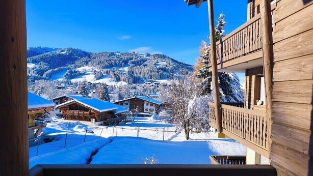 A wooden cabin with a balcony overlooking a snow-covered village and mountains. - Cozy apartment with pool and golf nearby (Megève)
