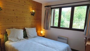A bedroom with a wooden headboard, a bed with white linens, a nightstand with a lamp, and a window with curtains. - Cozy apartment with pool and golf nearby (Megève)
