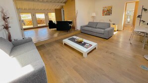 A spacious living area with a grey sofa, a white coffee table, and a wooden floor. There is a dining area visible through an open doorway. - Luxury View Terrace Apartment (Firenze)