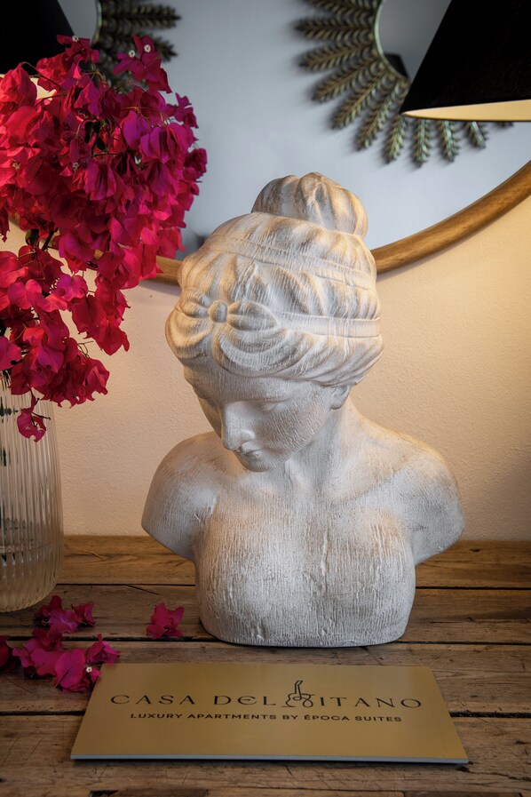 A bust sculpture on a wooden table with a brochure titled "CASA DELITANO LUXURY APARTMENTS BY ÉPOCA SUITES" in front of it.