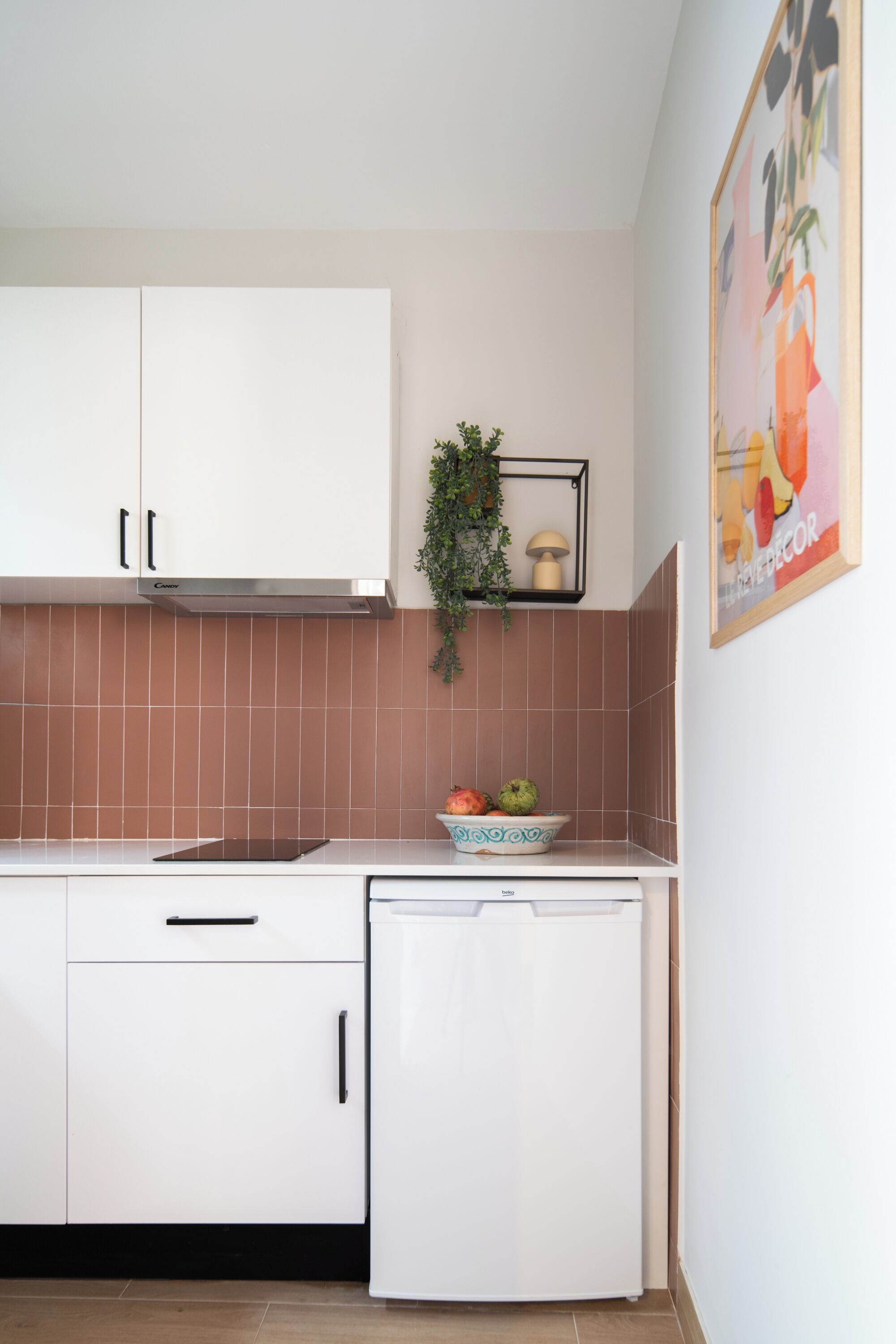 A kitchen with white cabinets, a small refrigerator, a sink, and a decorative plant.