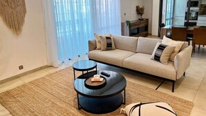 A modern living room with a sofa, two coffee tables, and a large window with sheer curtains. - Almadies Peaceful Oasis | 24/7 Security |Casa Molo (Dakar)