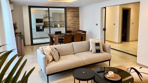 A modern living room with a sofa, coffee table, and a dining area with a table and chairs. - Almadies Peaceful Oasis | 24/7 Security |Casa Molo (Dakar)