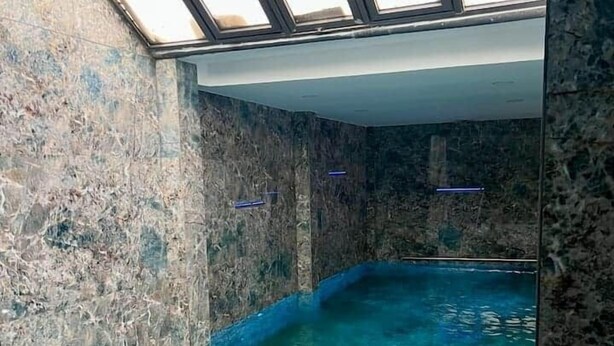 En swimmingpool med kristallklart blått vatten, omgiven av stenmurar och med ett takfönster ovanför.