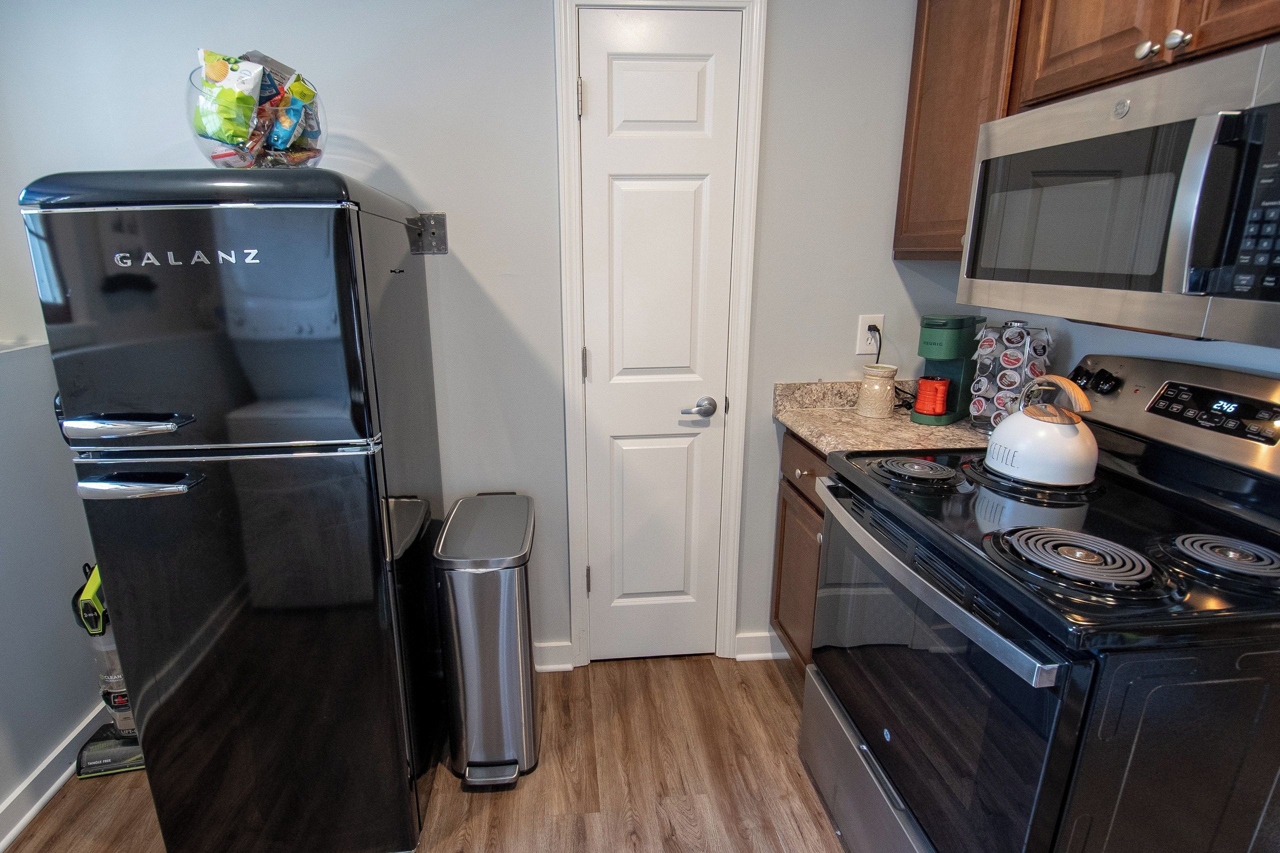 A compact kitchen with a black refrigerator, a microwave, a kettle, and a coffee maker.