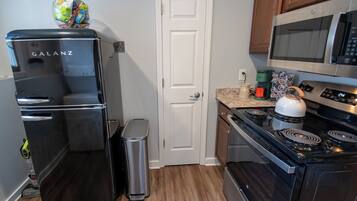 A compact kitchen with a black refrigerator, a microwave, a kettle, and a coffee maker.